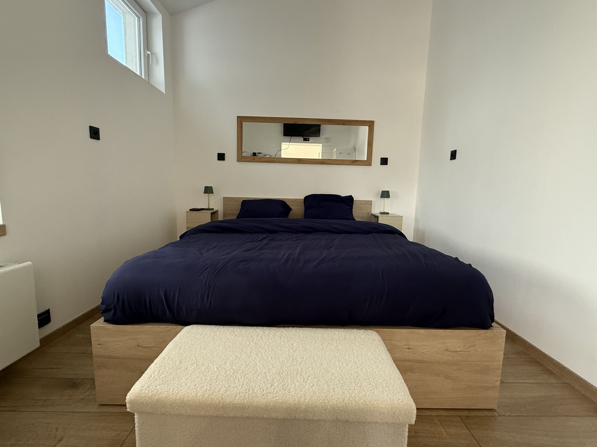 Chambre avec lit double, parure bleu nuit, chevets, lampes et banc au pied du lit