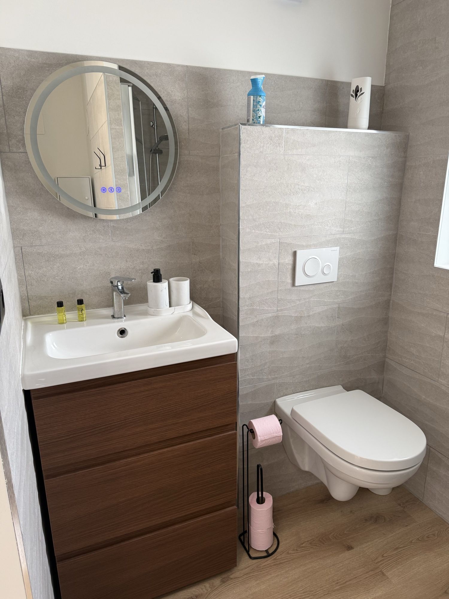 Salle d'eau : meuble vasque en bois, miroir rond lumineux, WC suspendu